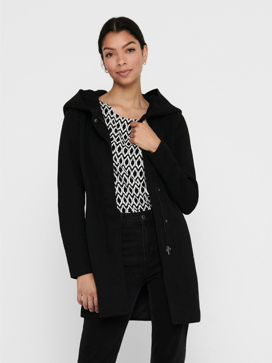 Woman wearing a black coat over a patterned top on a white background